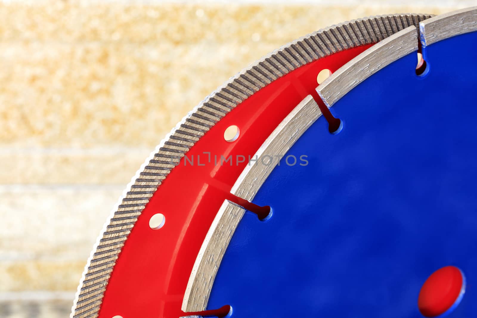 Red diamond cutting disc for granite and stone, blue for concrete, reinforced concrete against the orange-golden sandstone wall.