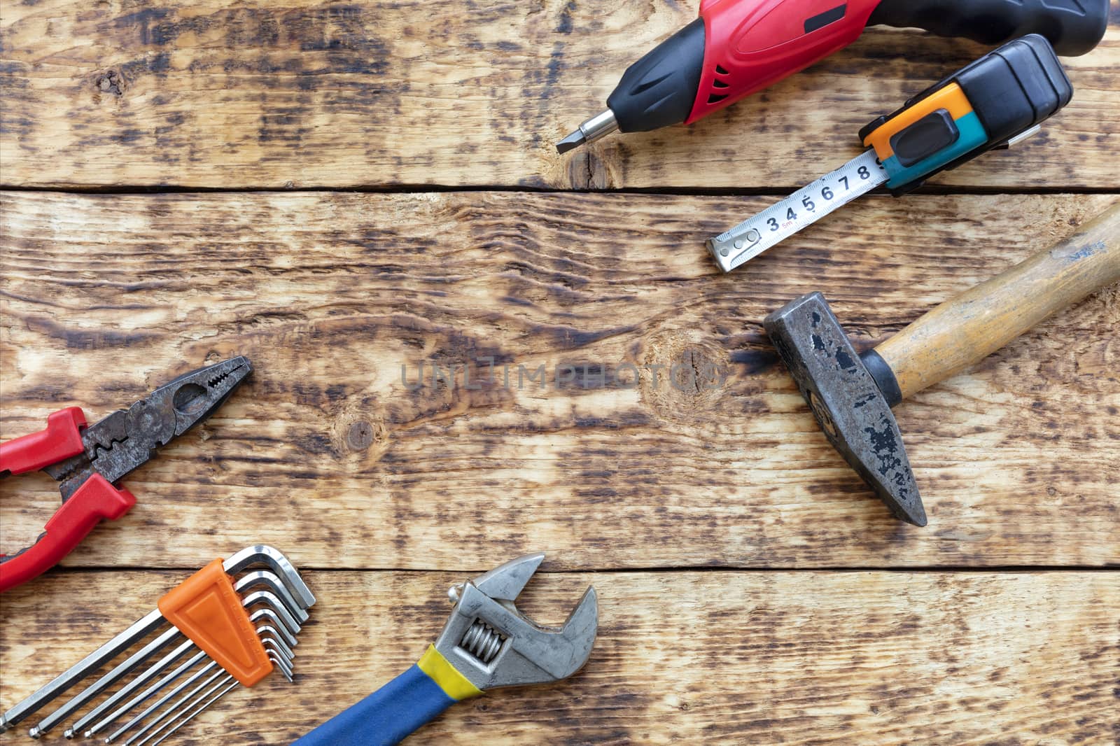 Old hand tools, pliers, hammer, tape measure, adjustable wrench, electric screwdriver, a set of hex keys lie on the old wooden table.