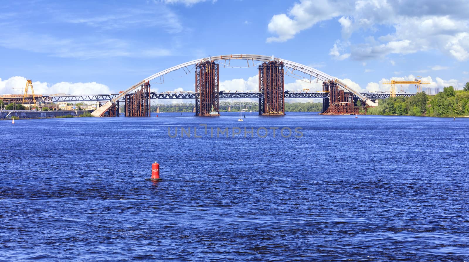 View of the blue waters of the wide Dnipro and the construction of a Podolsky bridge on the river in Kyiv.