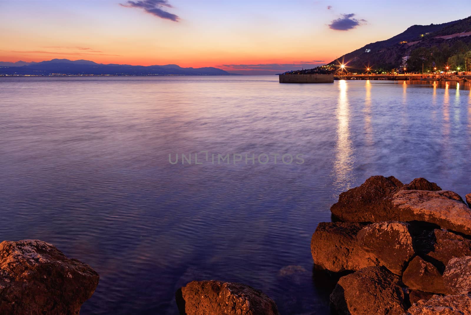 Beautiful, bright sunset on the Corinthian bay, cityscape promenade in the night city of Loutraki in Greece.