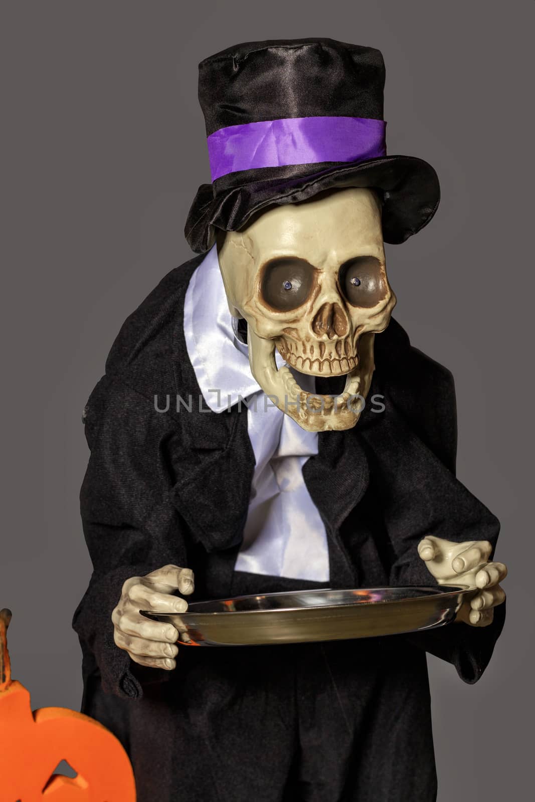 Halloween, doll Death in a black tailcoat and baggy hat with a metal tray in her hands came to collect tribute, isolated on a gray background.