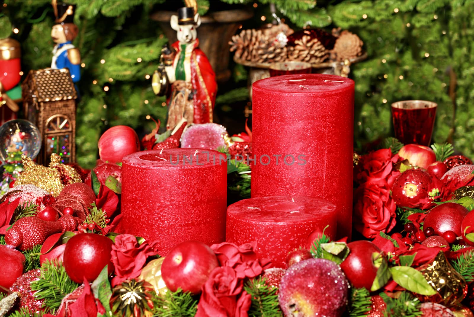 Christmas decoration: three thick red candles surrounded by blurry Christmas decorations and fairytale figures on the background of fir branches, close-up.