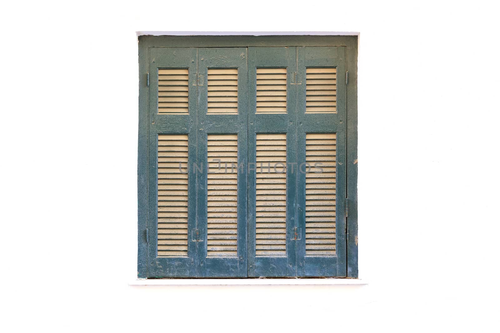 Light brown wooden shutters on an old green window against the background of a white facade of the house.