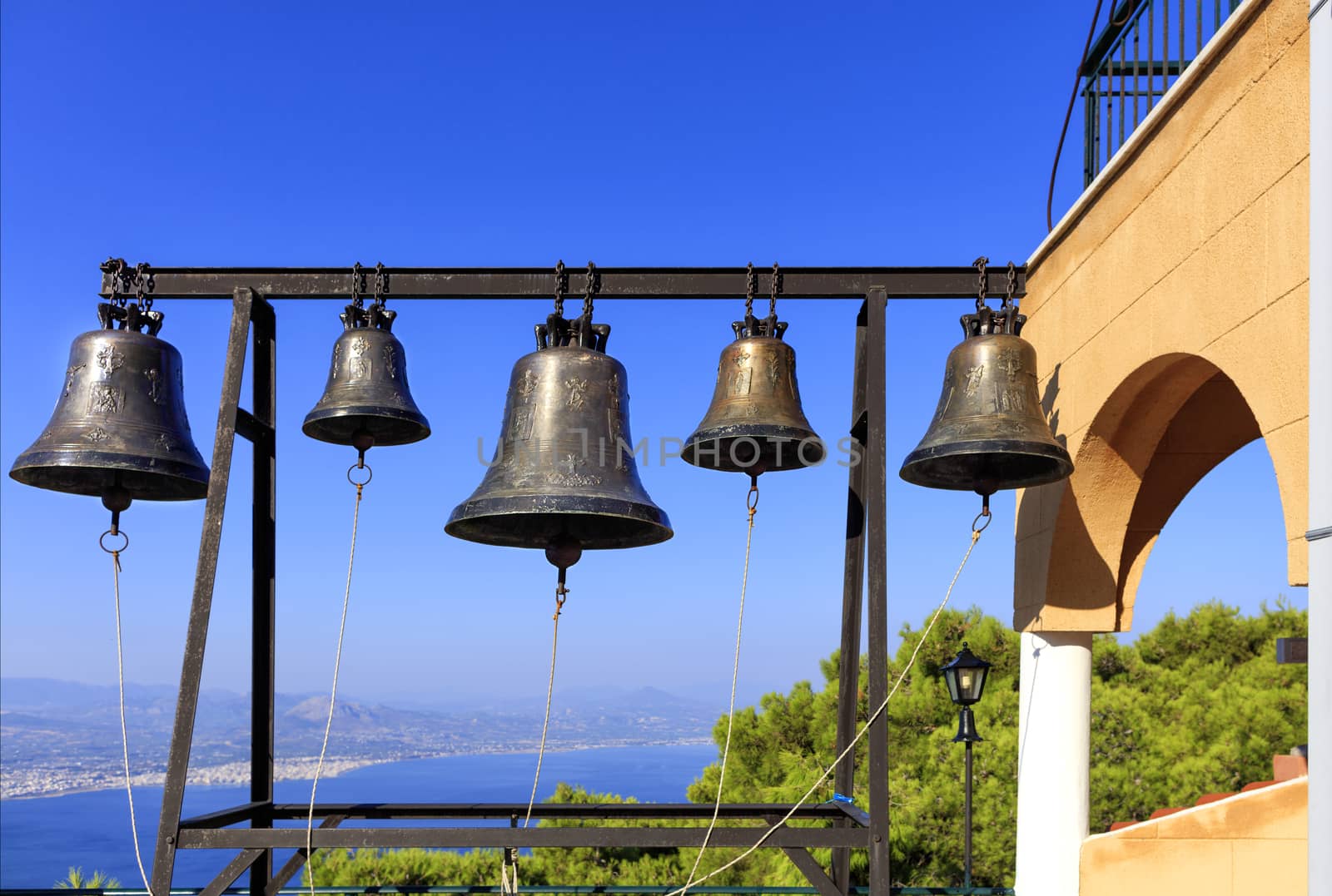 Closeup of bells against a blue sky, mediterranean pine and sea coast in blur, Greece, August 2019. by Sergii