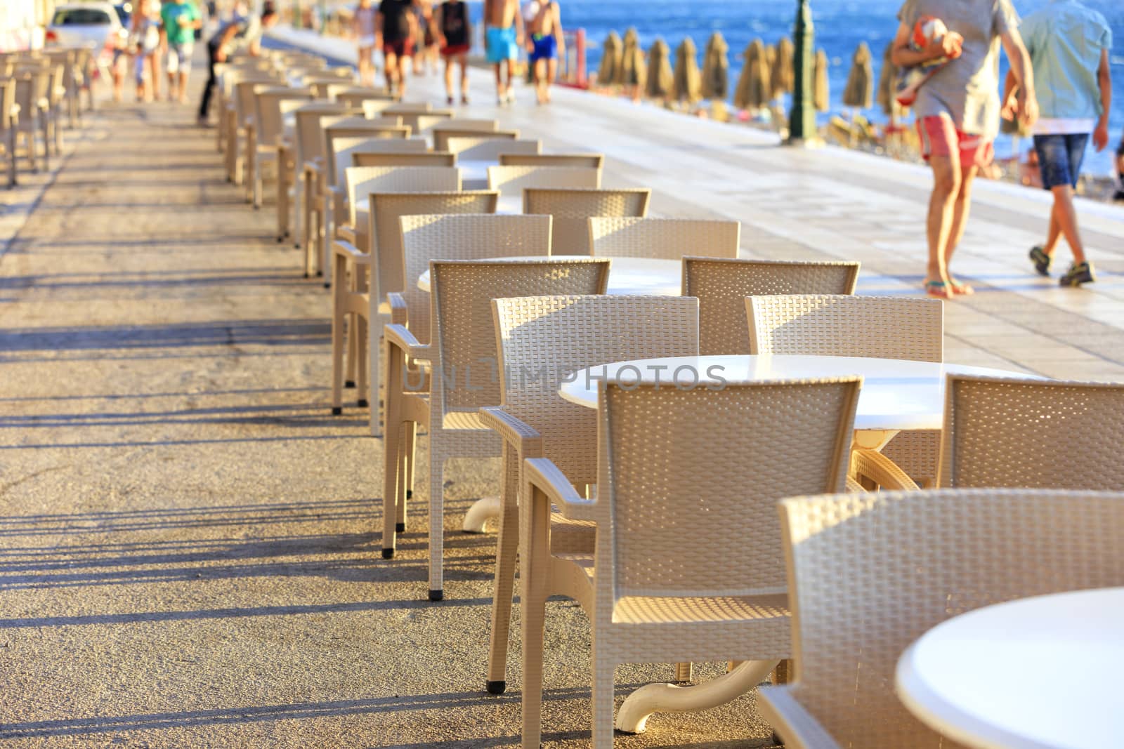 Tables and chairs of the beach cafe are located along the promenade where vacationers walk.