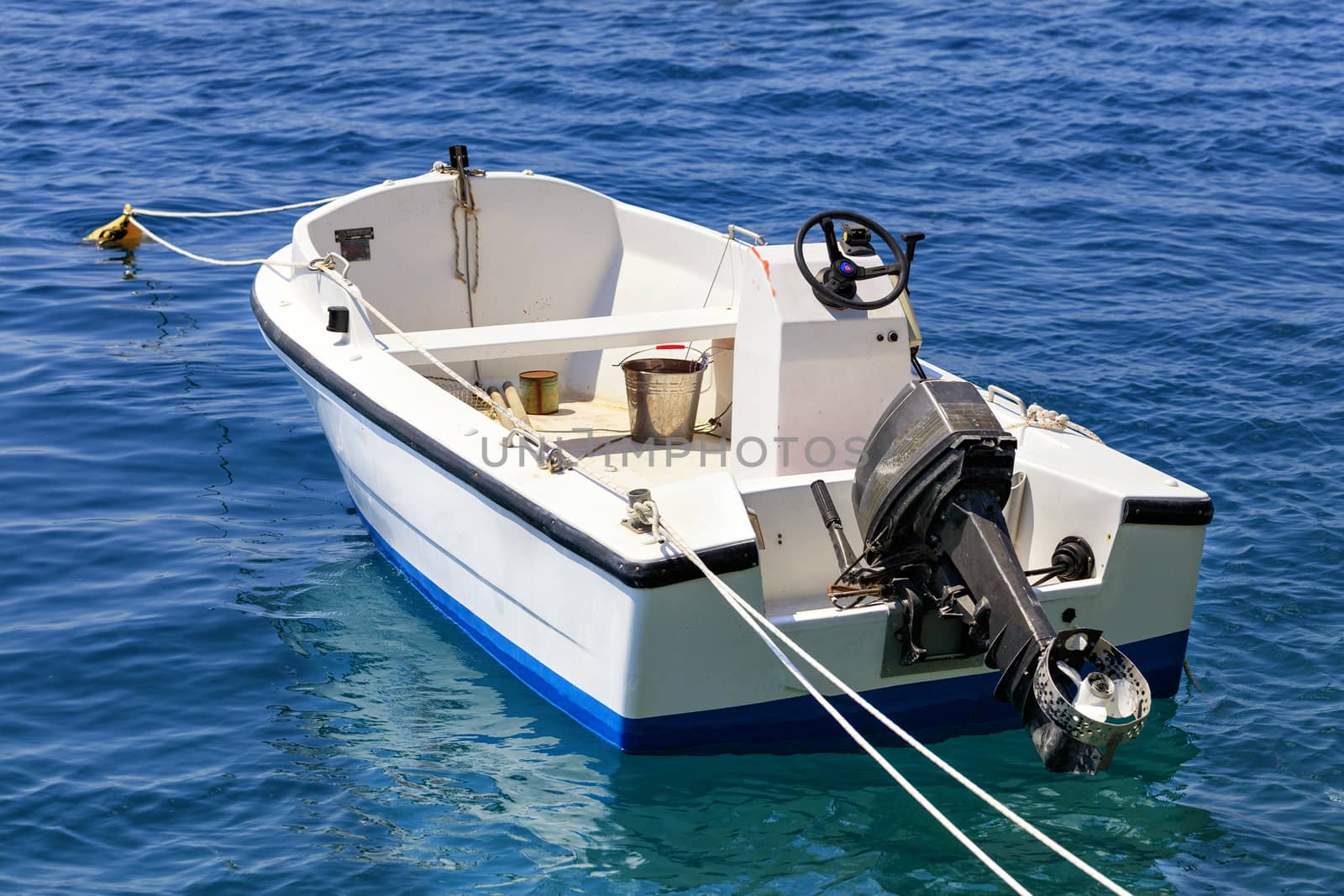 A fishing motor boat is anchored in the clear turquoise waters of the Ionian Sea with a raised engine. Loutraki, Greece.