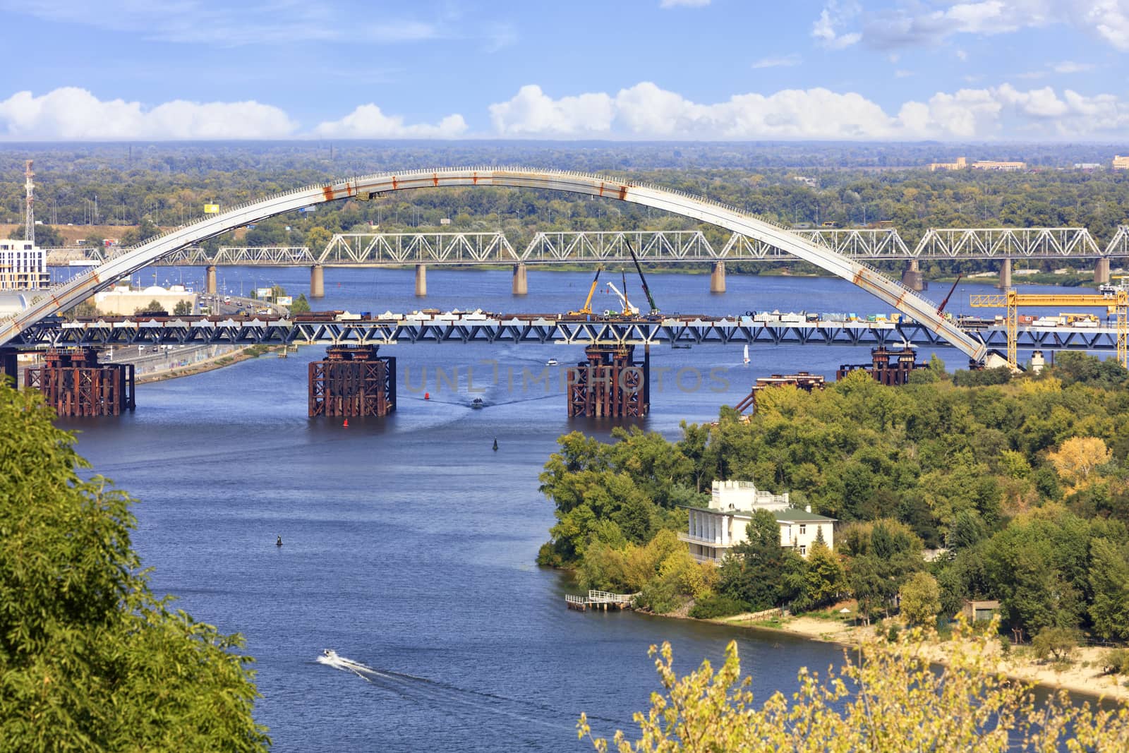 View of the blue waters of the wide Dnipro, the construction of the Podolsky bridge over the river in Kyiv, Trukhanov island, a bird's-eye view.