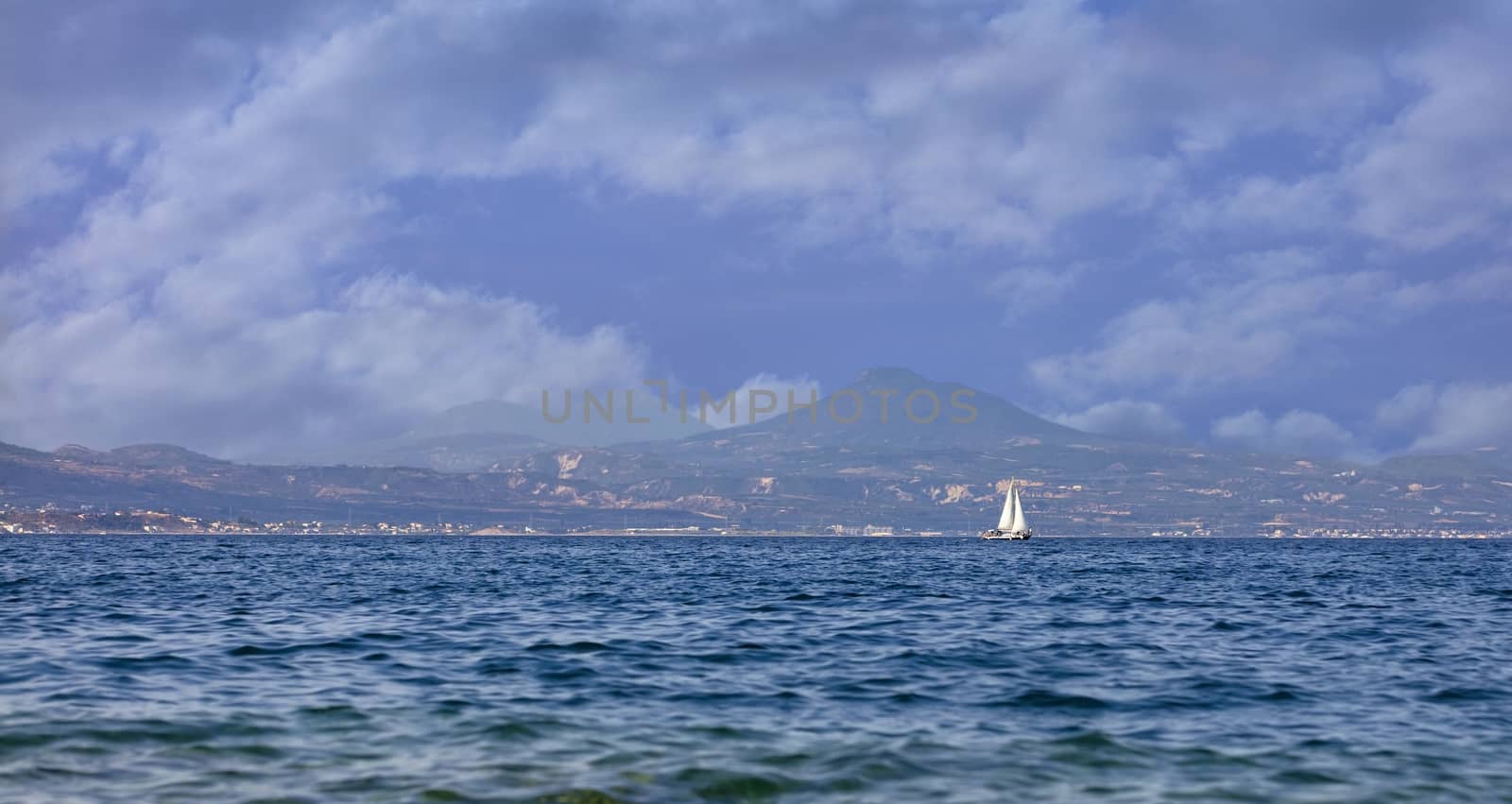 Silhouette of a sailing yacht on the horizon against the backdrop of Mount Acropolis in Corinth in the morning haze.