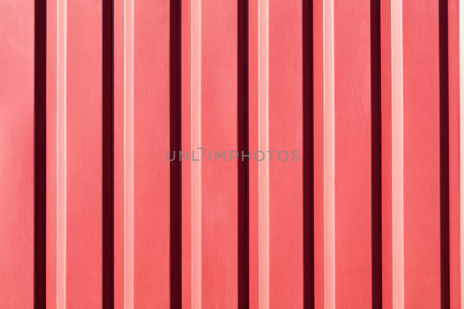 Red metal fence made of corrugated steel sheet with vertical guides and a soft sunny gradient.