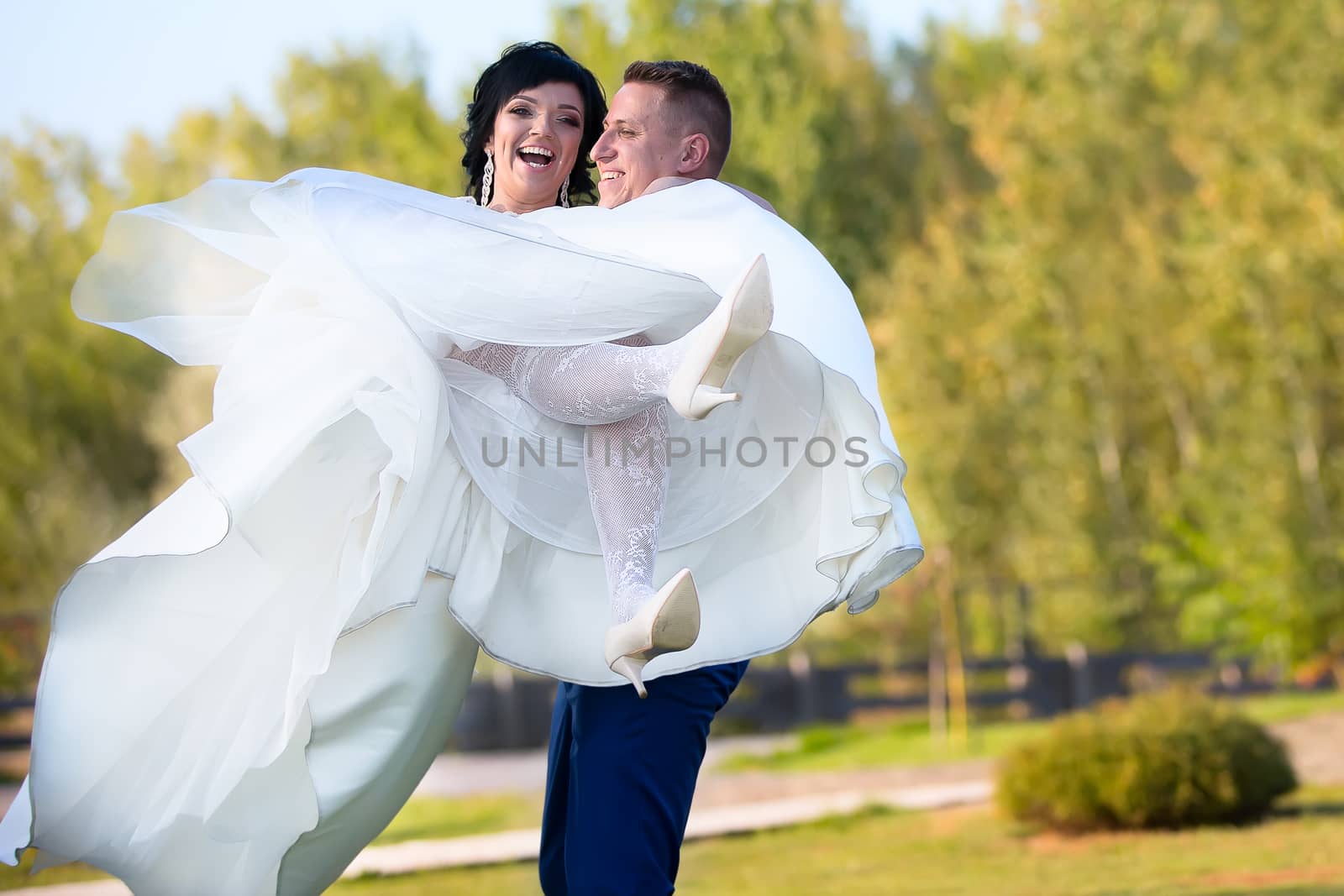 The bridegroom holds the bride in her arms.The bride and groom are happy