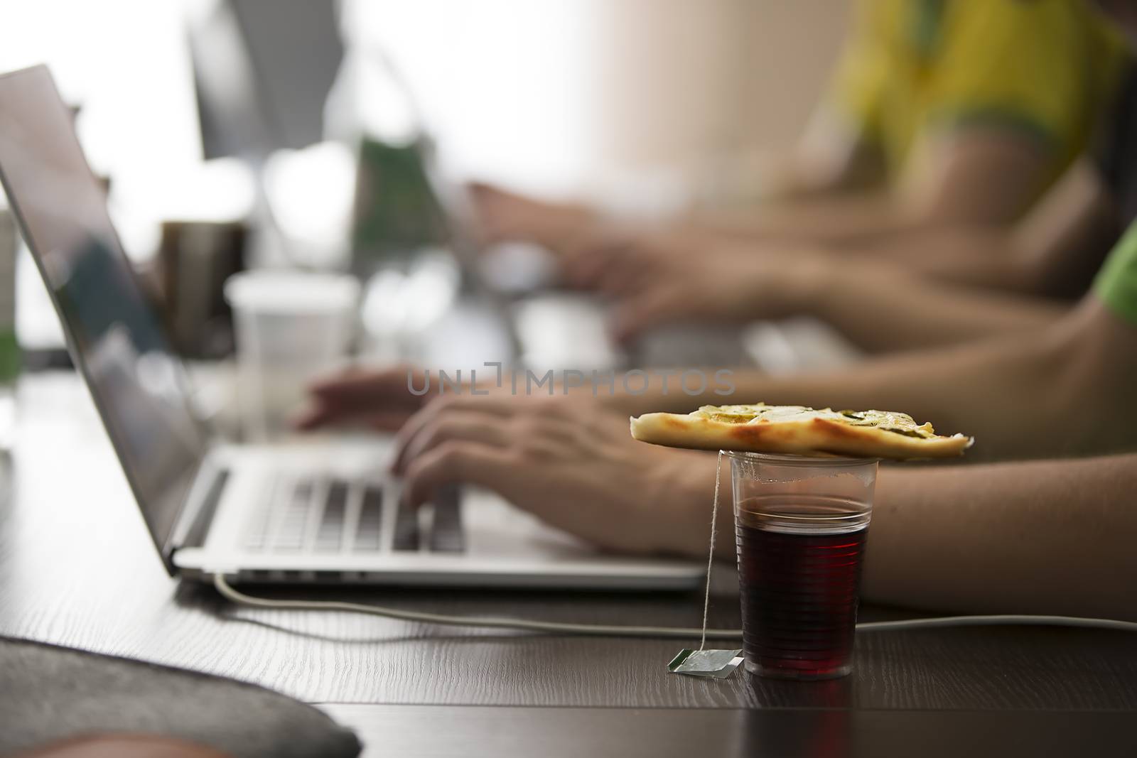 A plastic glass of tea and a piece of pizza on the table at the programmers. Lunch programmer.