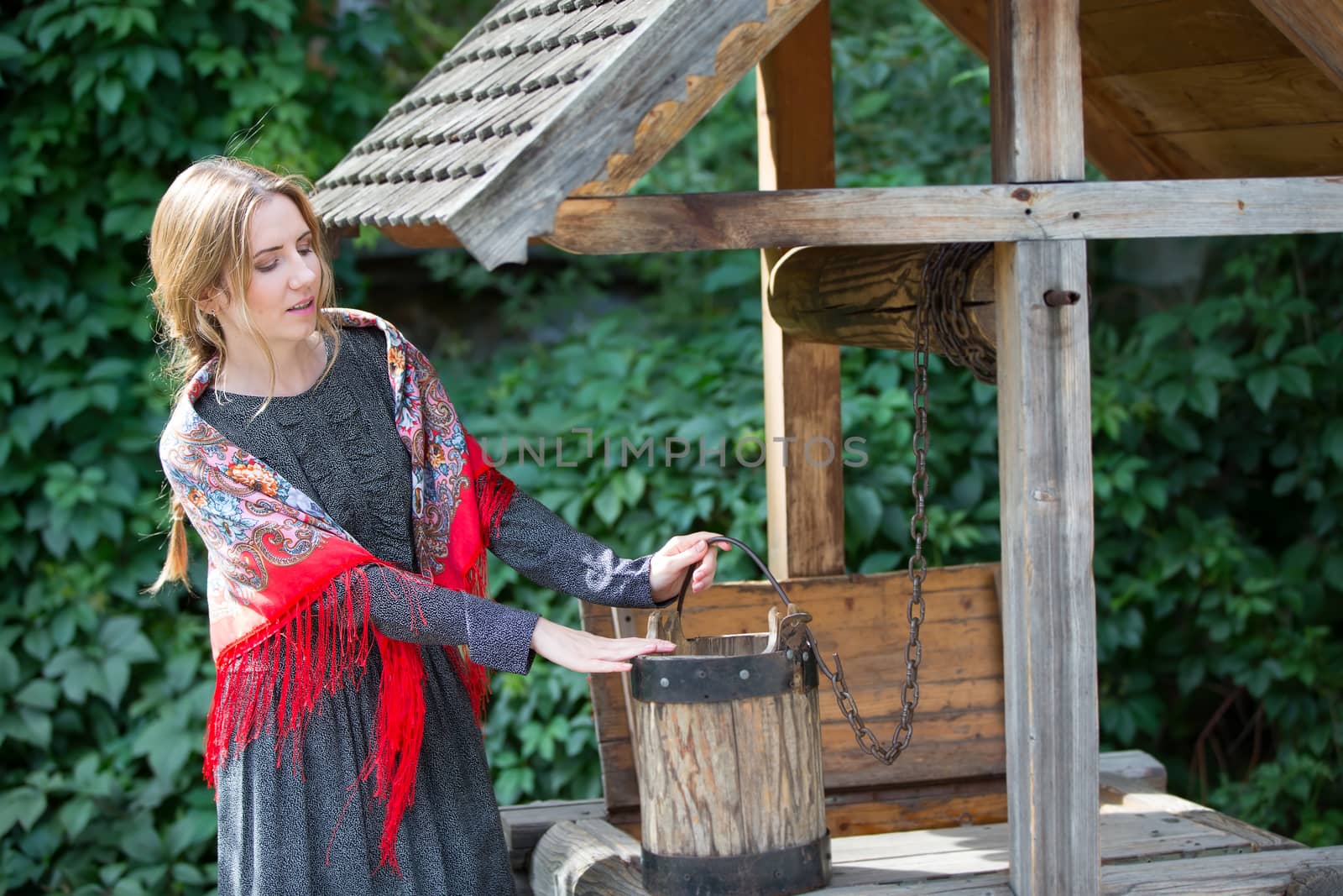 Russia, Moscow, Izmaylovsky Park, August 27, 2017. International Photo Festival.A Russian woman in a scarf with a bucket at the well. Russian woman. A woman with a Russian handkerchief.