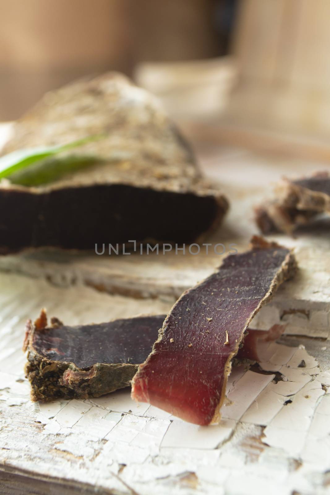 Sliced venison steak, dry meat of wild roe on rustic wooden board, vertical image