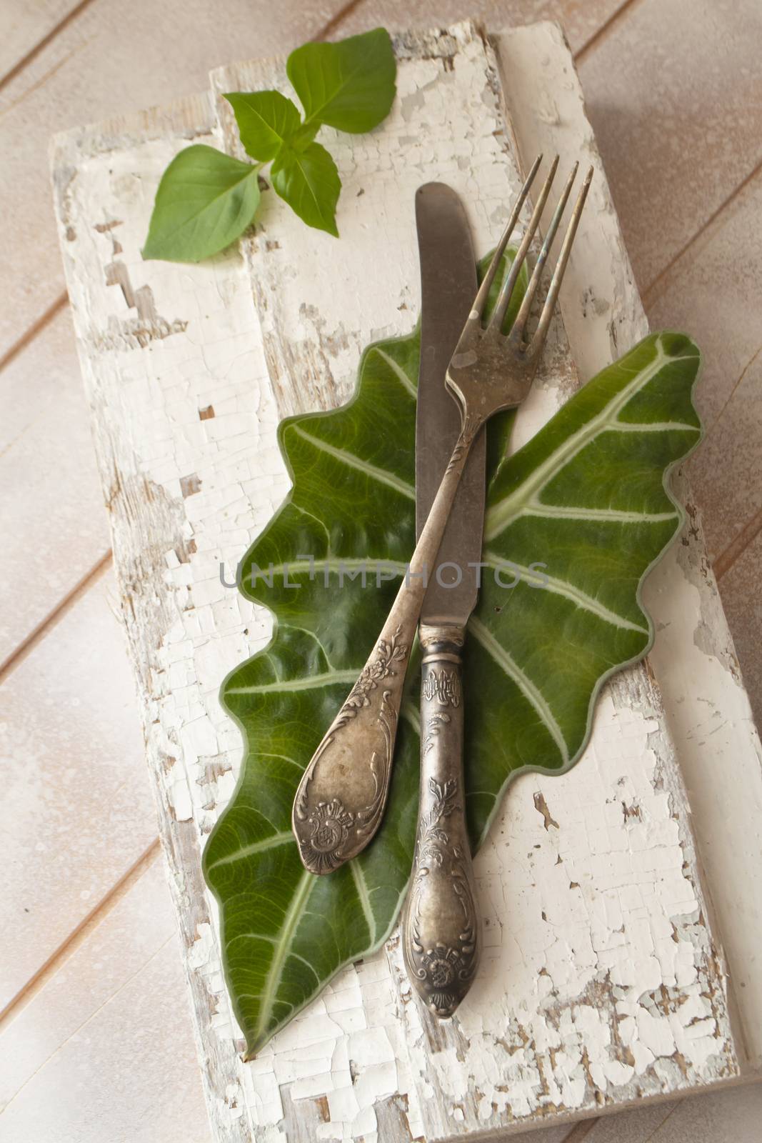 Fork and knife on wooden board with fresh basil leaves, vertical image