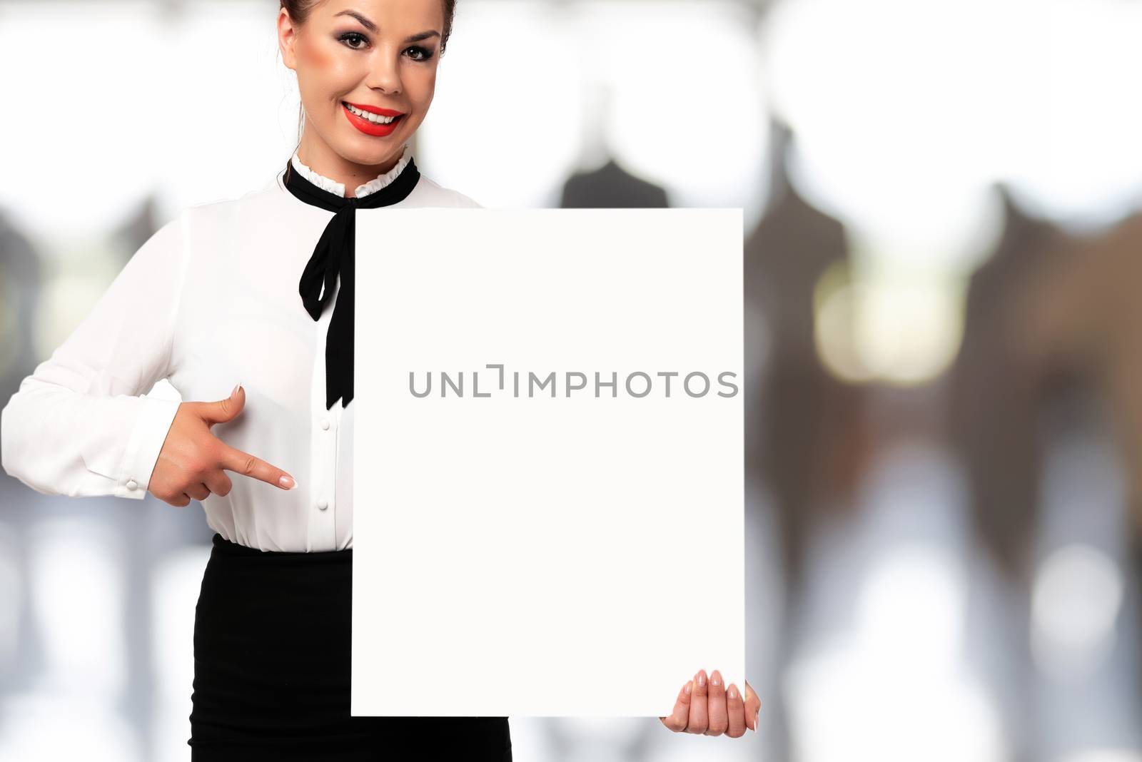 Beautiful business woman smiling and holding a white sign board with copy space for advertising and text on a blurred background of the office.