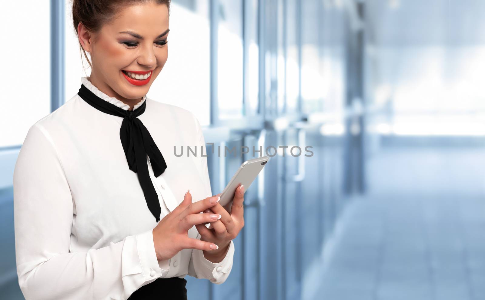 Modern communication concept - attractive business woman holds smartphone and enjoying video calling transmission on a background of corporate building (copy space)