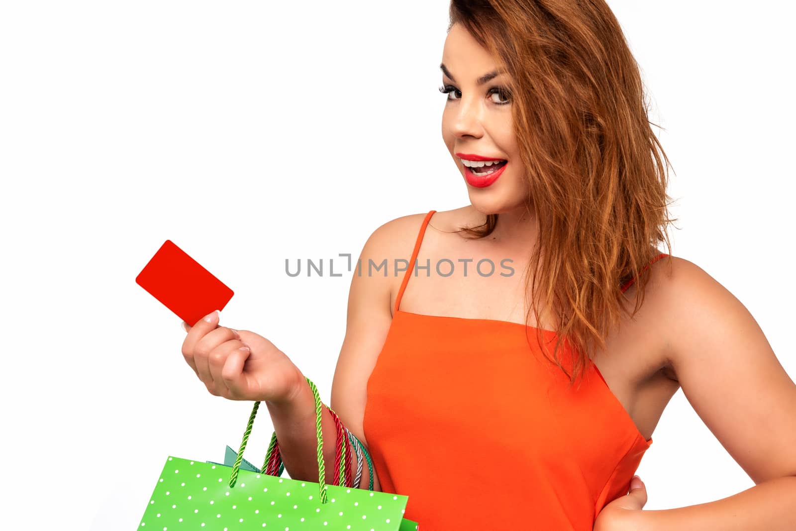 Beautiful woman in an orange dress holds a blank gift card in her hand and enjoys the shopping