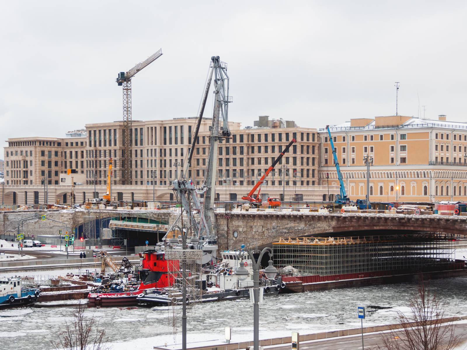 Ships with construction equipment are in Moscow-river under the bridge. Reconstruction of Bolshoy Moskvoretsky Bridge. Winter cloudy day in Moscow, Russia.