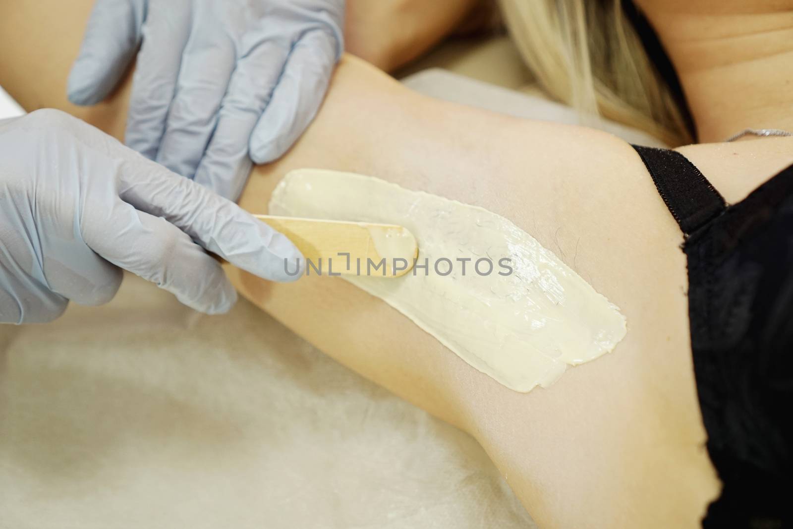 Waxing woman armpit with spatula. Salon wax beautician epilation procedure. Waxing female body for hair removal by therapist close up
