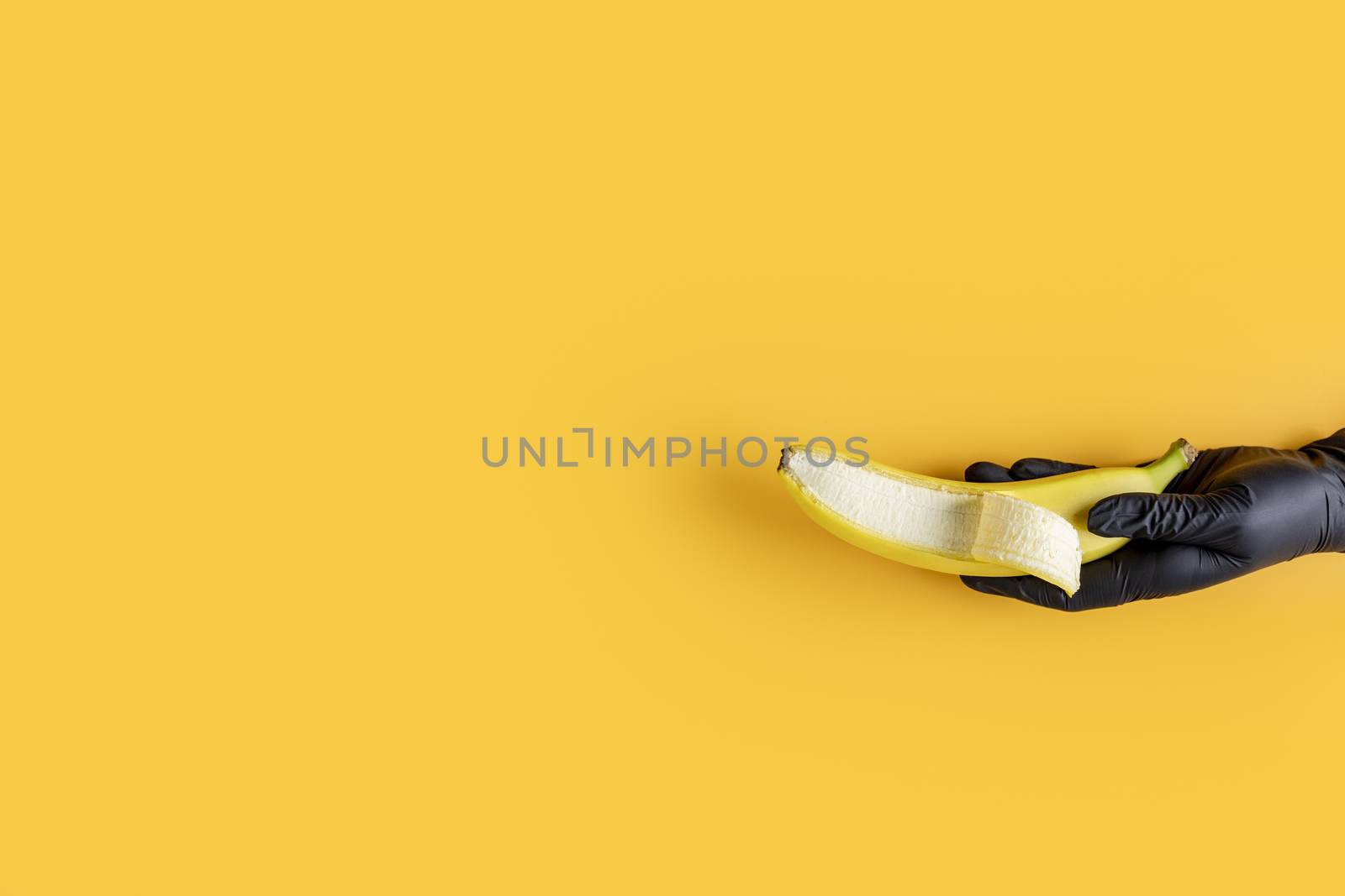 Hand in black glove holds banana on yellow background. Food art. by ArtSvitlyna