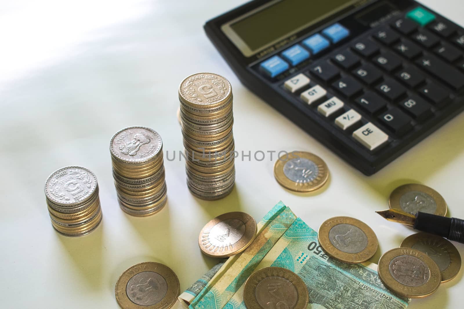 Bunches of five rupee coins are in three different stacks. A calculator and some notes and ten rupee coins are present