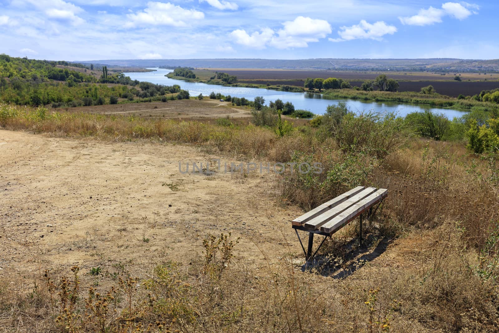 Autumn panorama landscape, sunny day. The edge of a country road near a wooden bench, which stands on a high bank of the river.