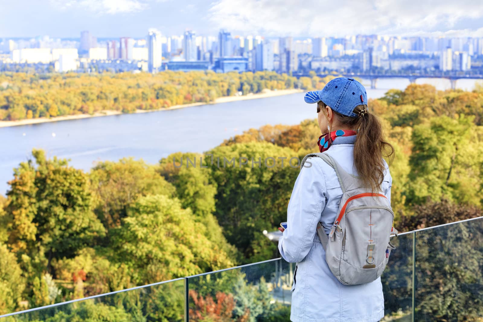 The traveler looks at the autumn cityscape of Kyiv with a view of the blue waters of the Dnipro River, Trukhanov Island and residential quarters of the left bank in blur. by Sergii