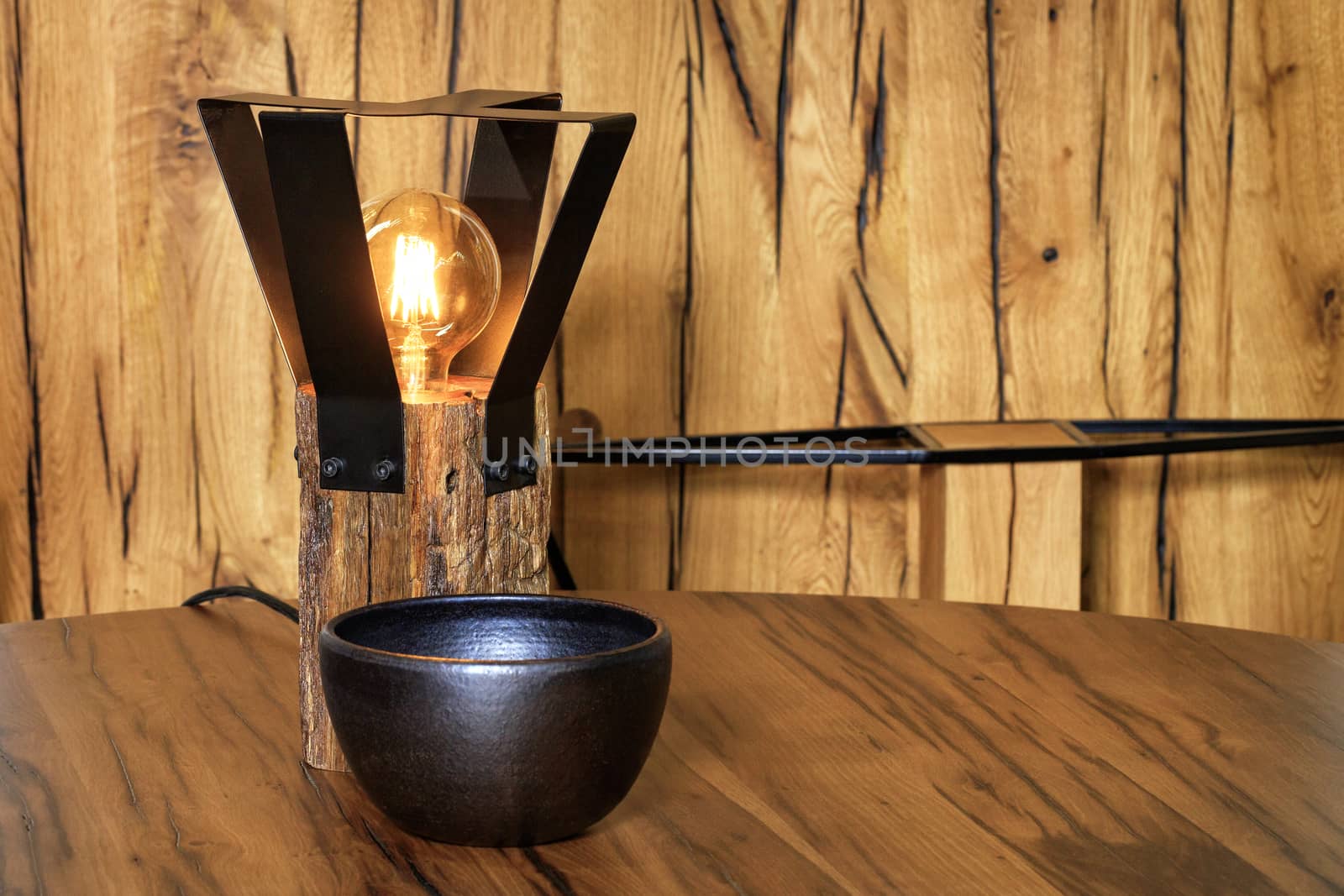 Original lamp from an old wooden bar and a protective metal grill around the lamp and a black clay bowl on a wooden table and an old cracked wooden background.