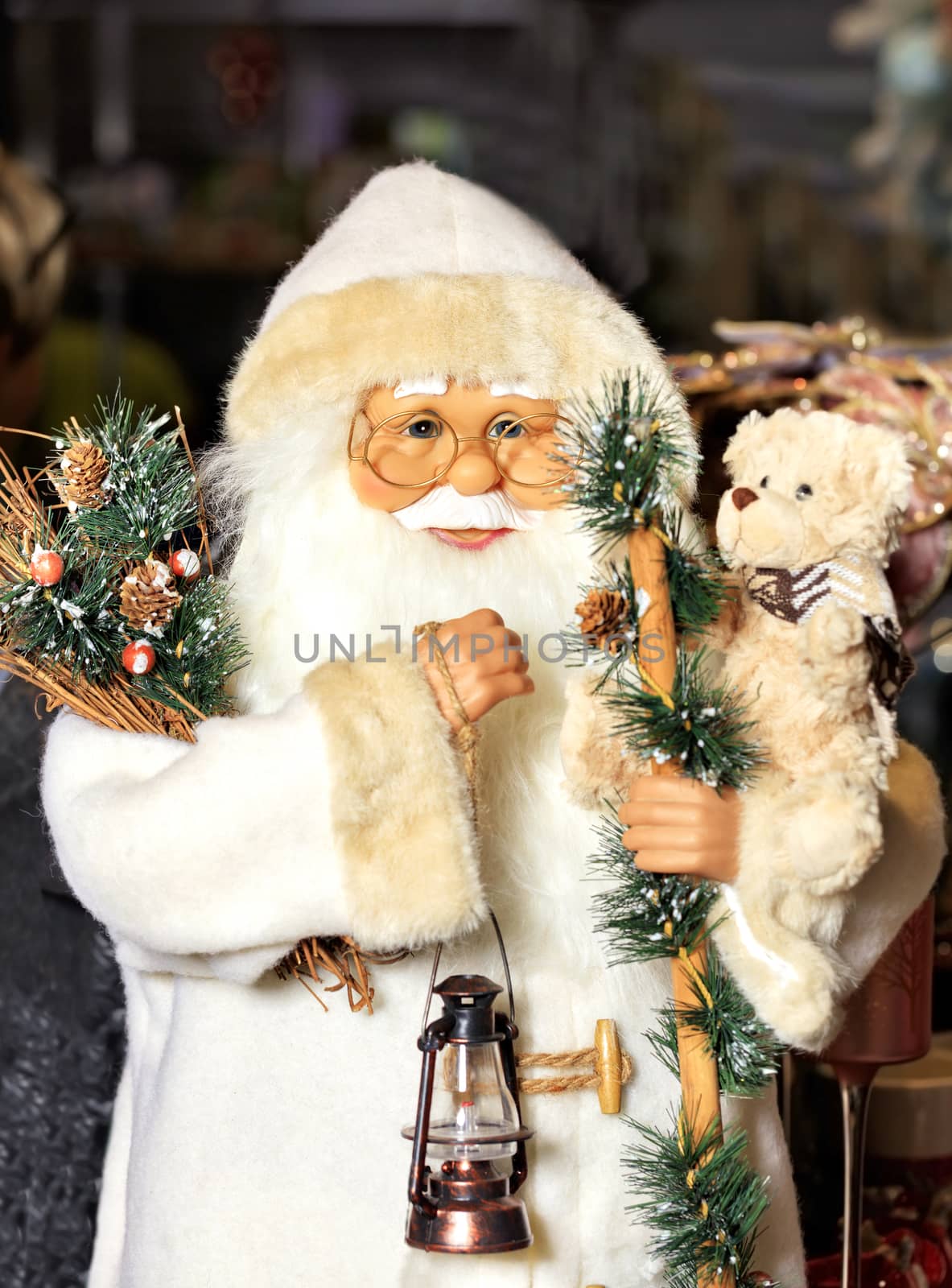 Decorative toy Santa Claus in a white fur coat with fir branches, cones, an old lamp in his hand and a little teddy bear. Marry Christmas concept.