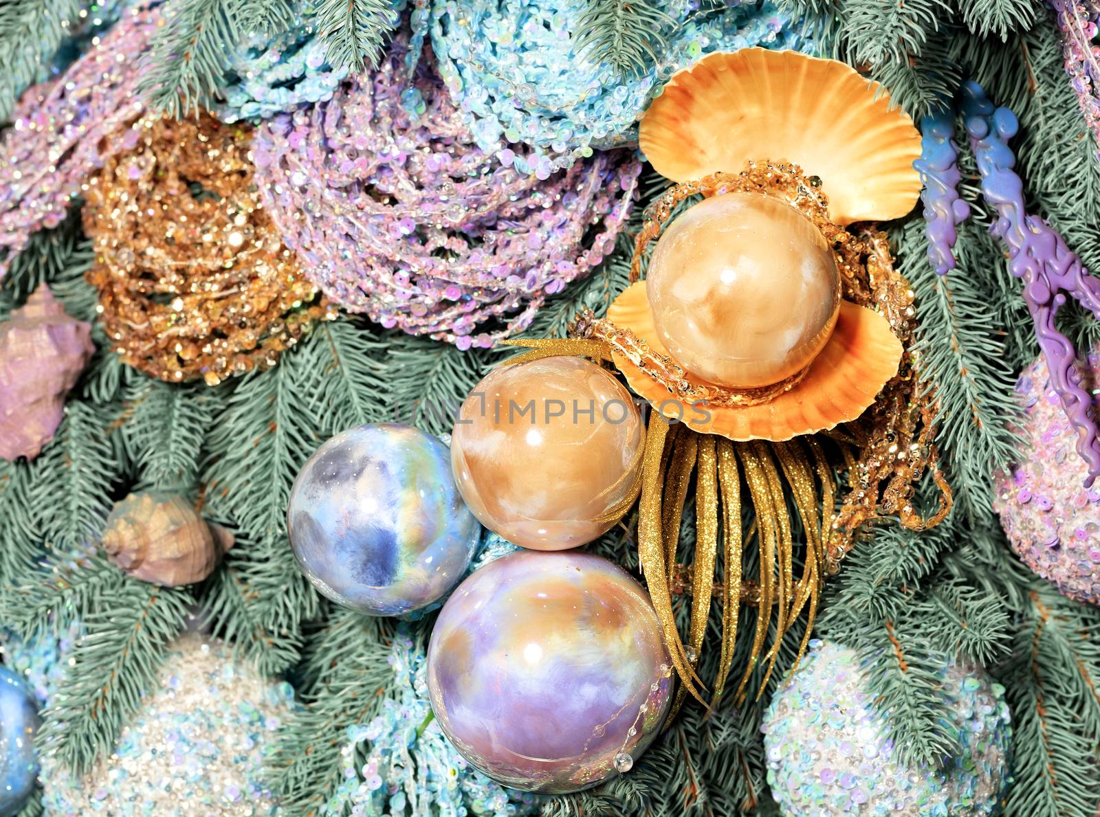 Christmas decorations in a marine style closeup. Glass Christmas baubles in shape of sea large pearl balls with gold, pink and blue tint hang on the decorative branches of the Christmas tree.