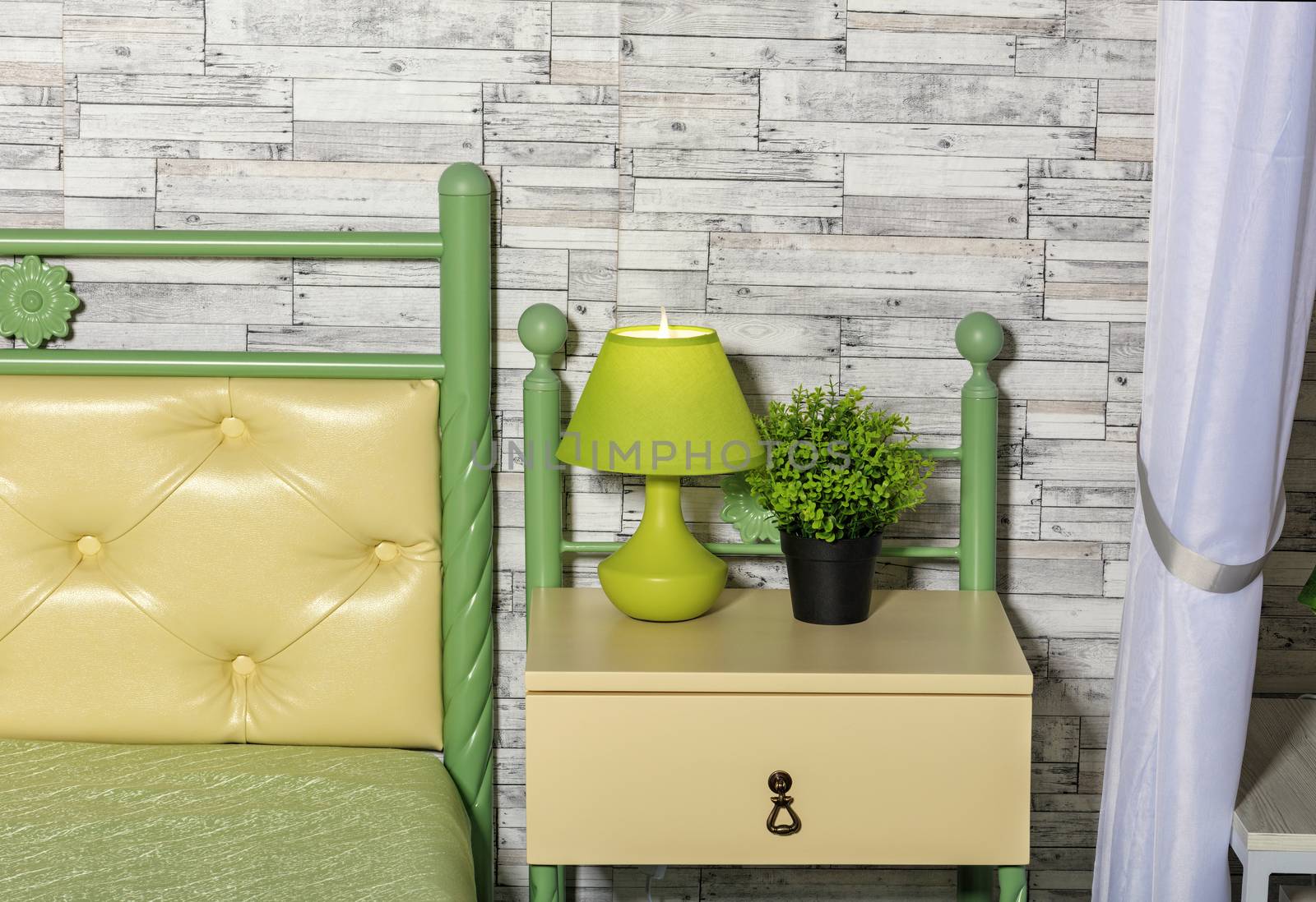 Fresh pastel green and yellow tone of the bed, a green flowerpot, an elegant table lamp on a yellow bedside table perfectly combines on a gray wall sphere of old wooden planks.