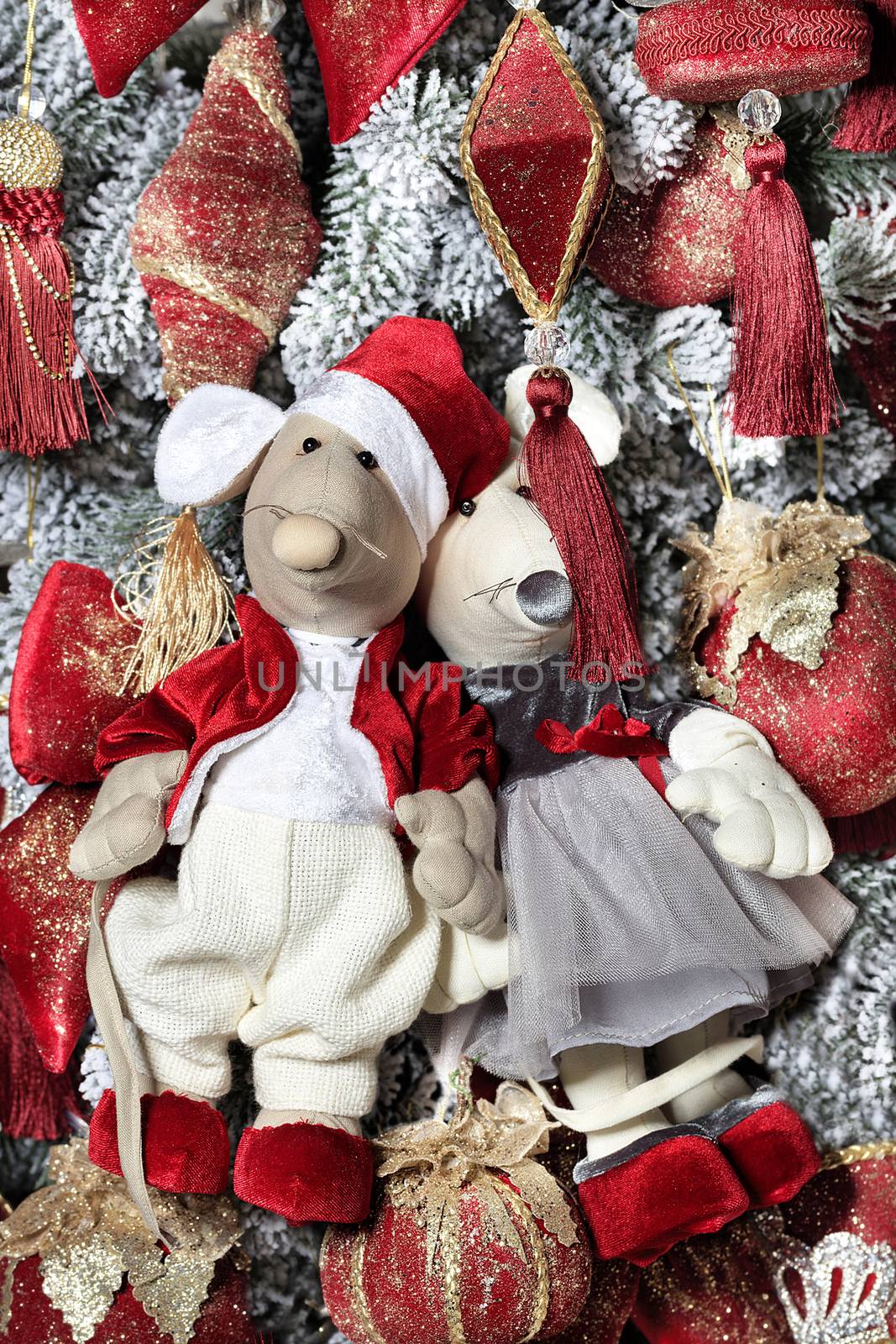 Little decorative toy mice dressed in a red frock coat and elegant dress are hanging on a Christmas tree on the eve of the rat year. New Year celebration concept, 2020 symbol, close-up view.
