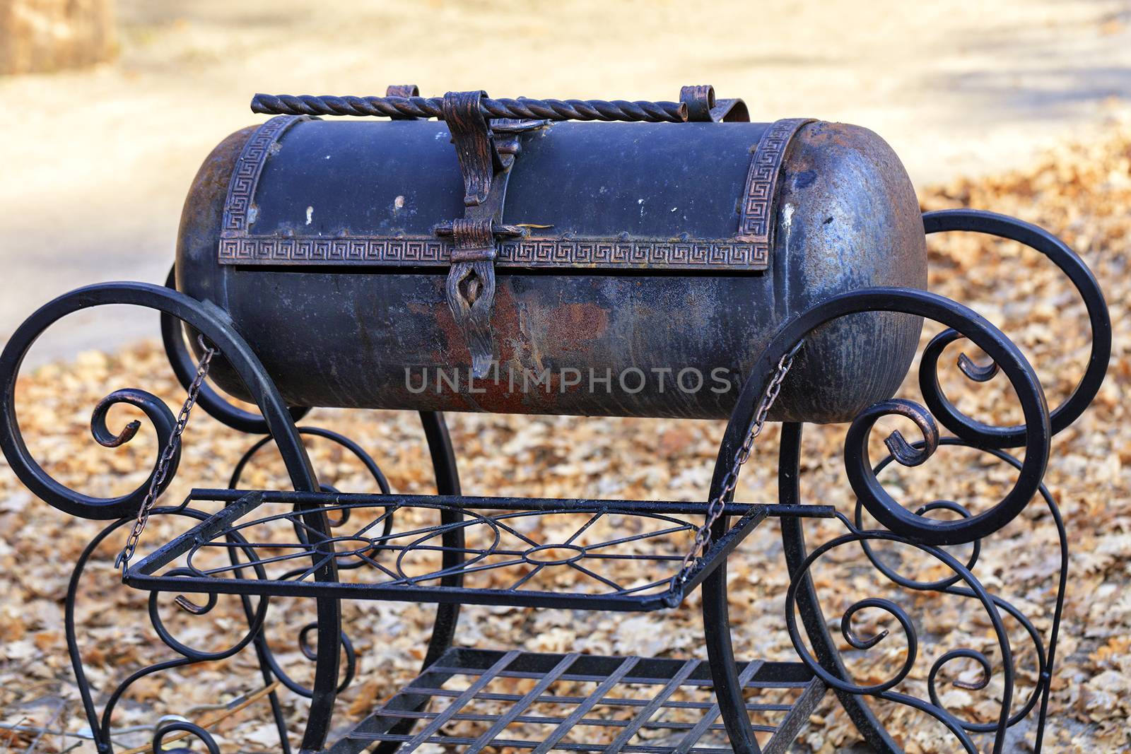 Nice old metal brazier with twisted curly handles made of wrought iron with a beautiful pattern on the background of autumn fallen leaves on a sunny day in blur.