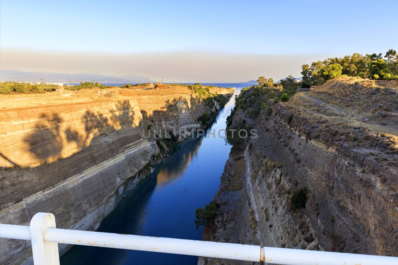 The Corinth Canal on a morning summer day illuminates the bright rising sun in Greece, a view of the Gulf of Corinth from the height of a pedestrian bridge. ??????????? ????????? ????????? ???? ? ?????????? ????? ??????????? ????.