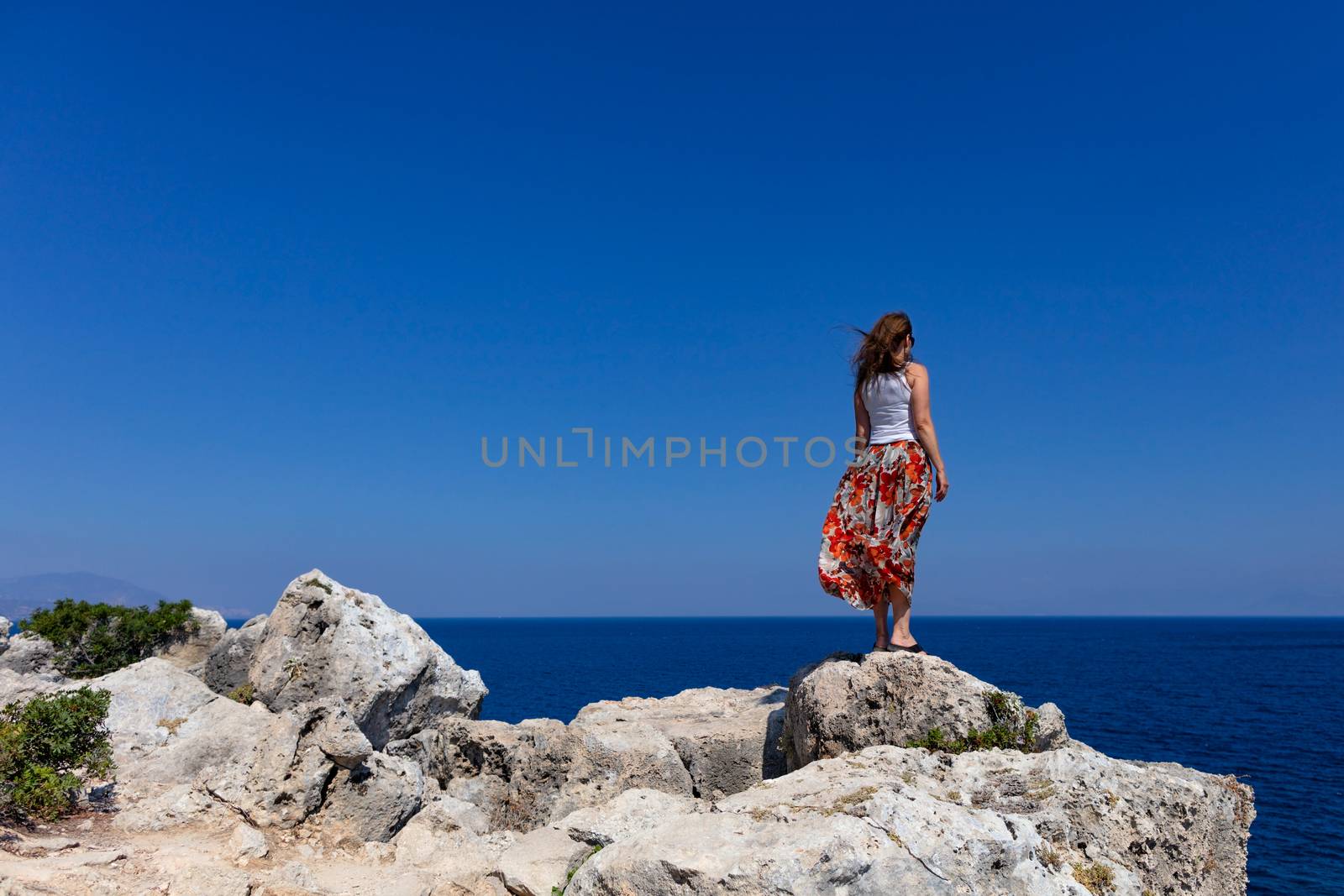 Lady stands on the edge of a stone cliff and looks into the distance to the sea horizon. by Sergii