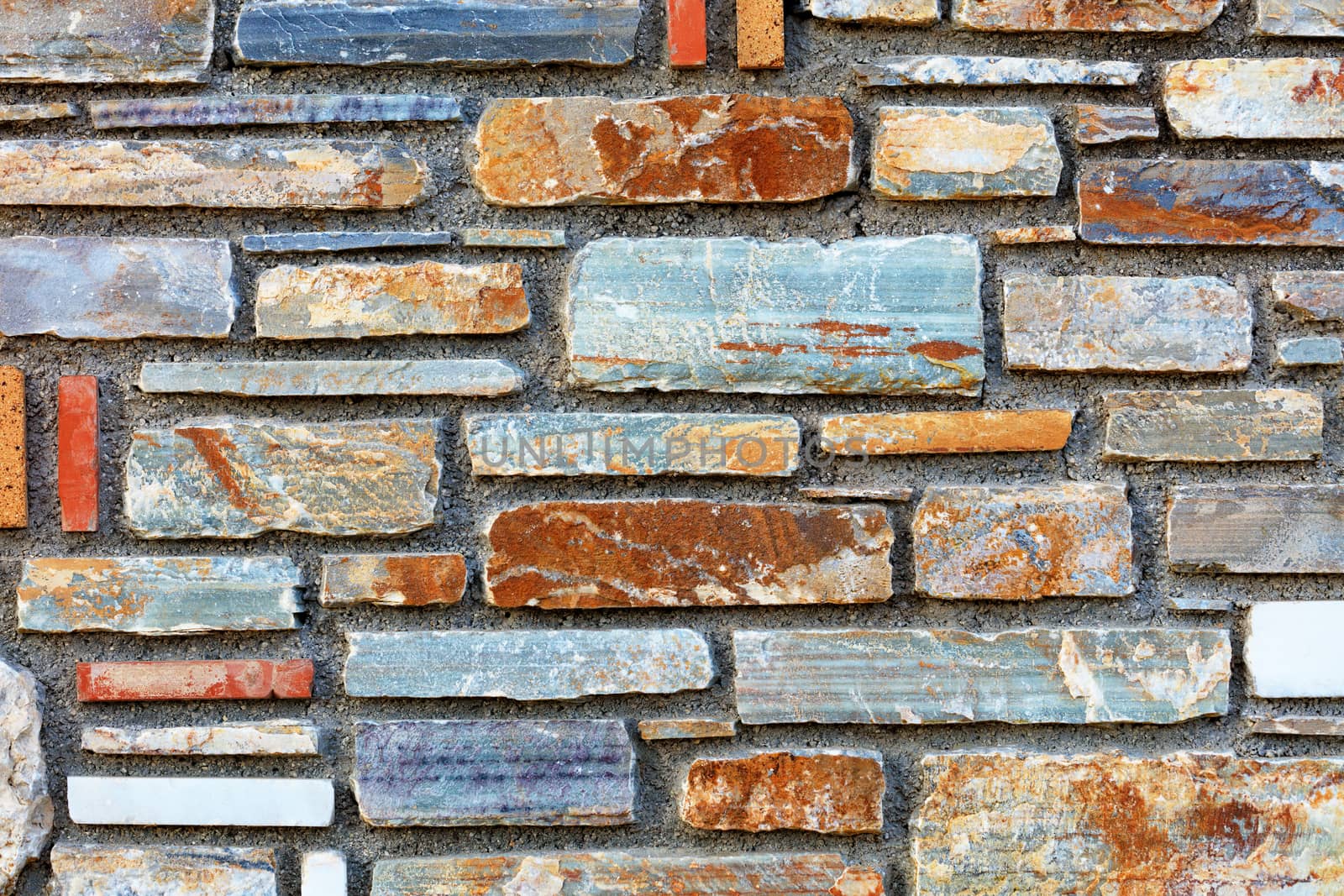 Stone mosaic of brown, blue, gray, white, green, orange stone blocks laid parallel to each other and form a stone background and pattern, surface with cement.