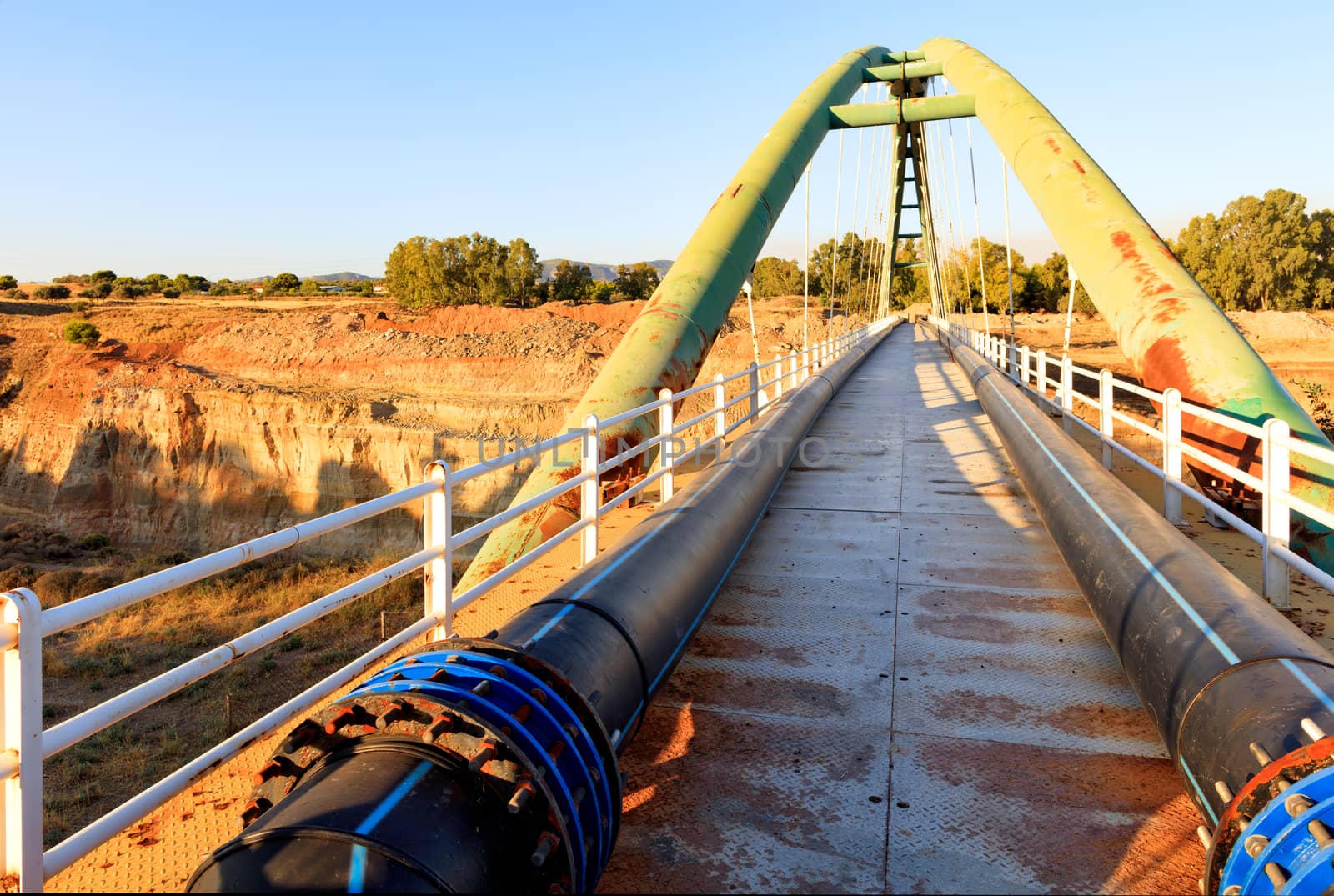 Pedestrian bridge on a bright sunny morning through the Corinth Straits, with engineering communications in the form of polypropylene pipes and iron fittings, image with copy space.