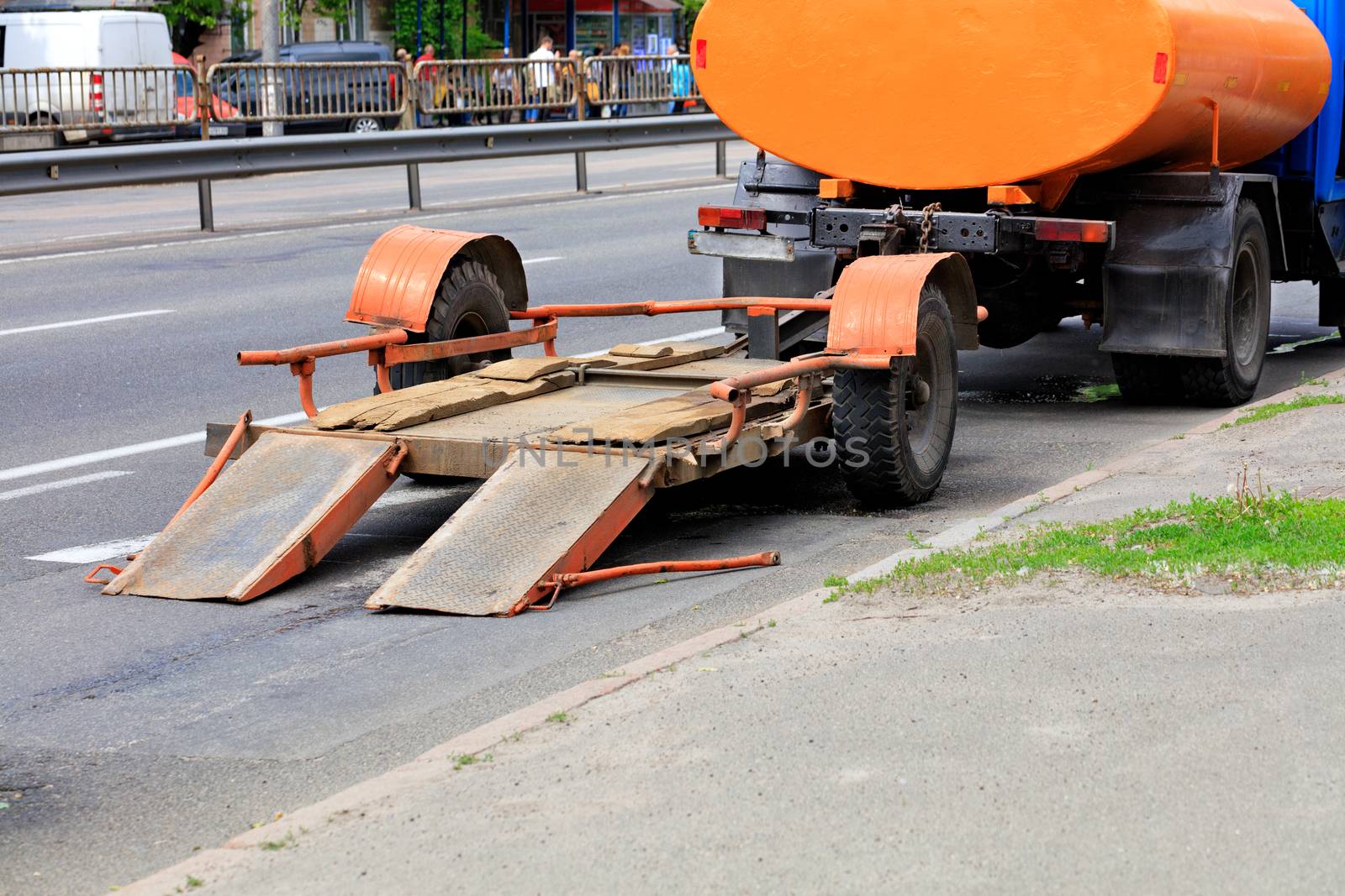 An old trailer with a low platform for transporting road equipment is attached to the rear bumper of an old water carrier truck, image with copy space.