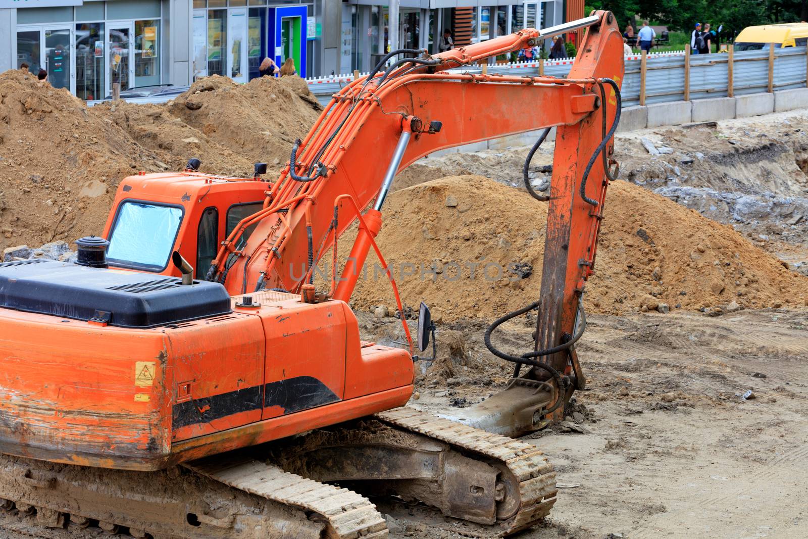 Heavy crawler construction excavator digs trenches for urban utilities at a construction site during road repair on a city street on a summer day, image with copy space.