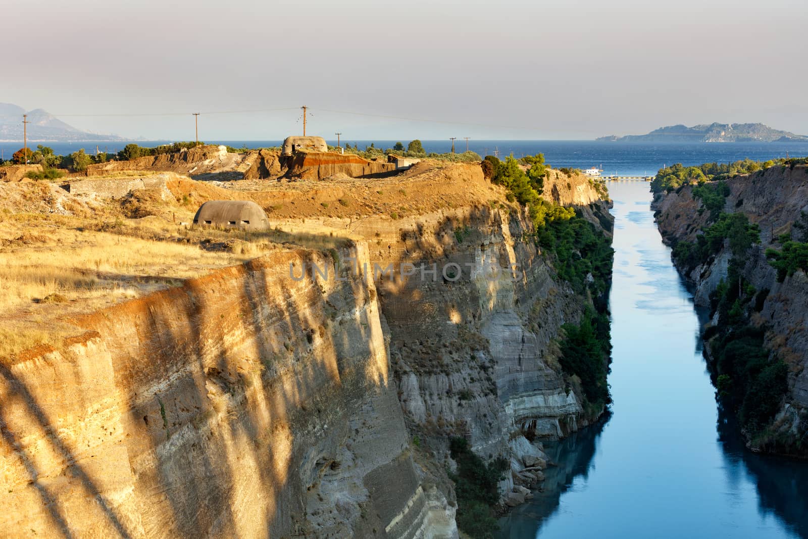 Coastal fortifications of the Corinth Canal in Greece in the bright rays of the rising sun and the horizon in the morning sea haze, image with copy space.