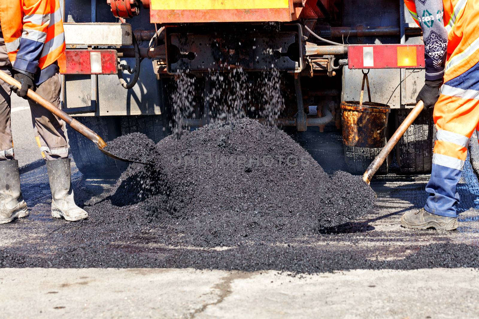 The working team sprinkles part of the asphalt with shovels to update it in road construction. by Sergii