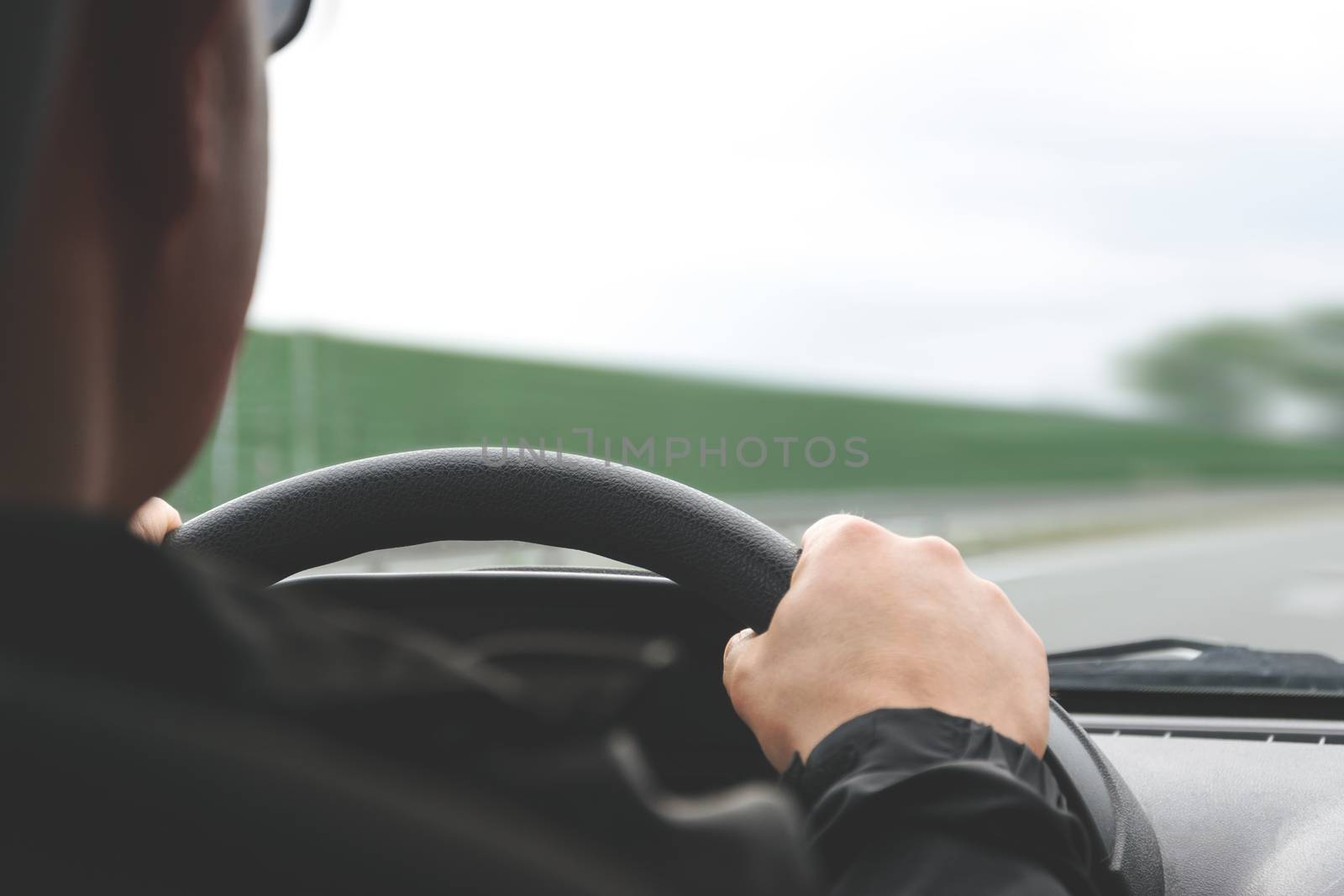 Close-up on male hands on the steering wheel of a car on a blurred background of the highway (reduced tone effect)