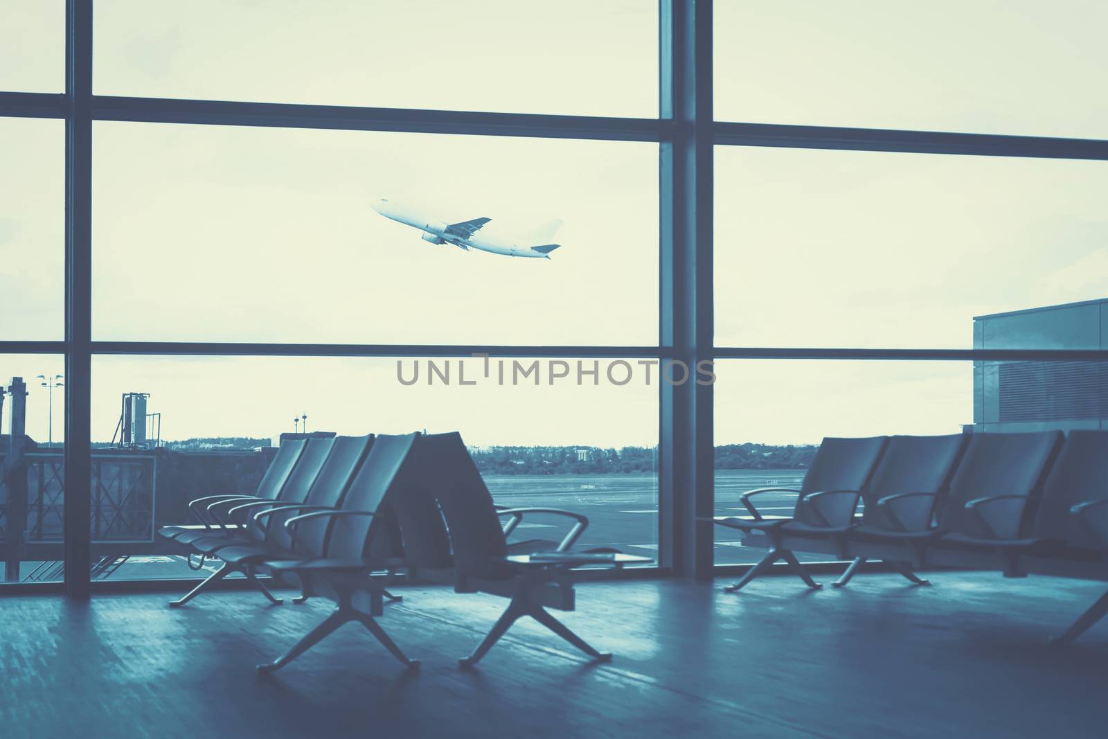 Traveling concept - empty interior of the airport lounge on the background of flying aircraft (blue filter effect)