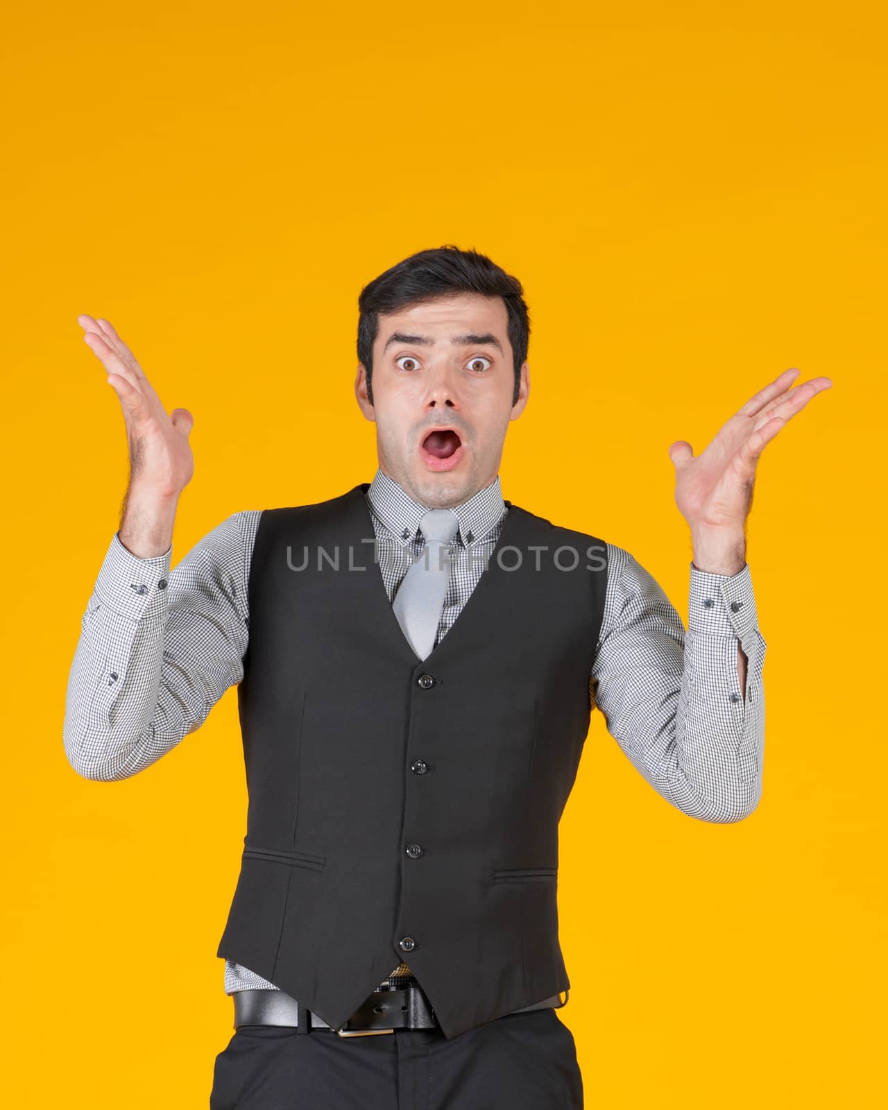 A businessman in a gray shirt and a black vest, raise both hands up with a surprised expression. The young man was shocked and gasped his eyes open.