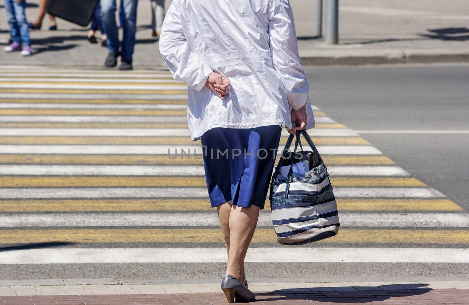 elderly woman is waiting to cross the road on sunny summer day