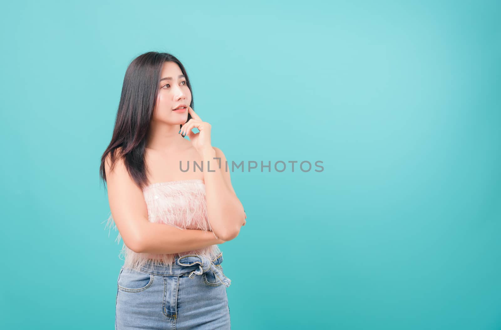 Asian happy portrait beautiful young woman standing thinking looking and looking to side isolated on blue background with copy space for text
