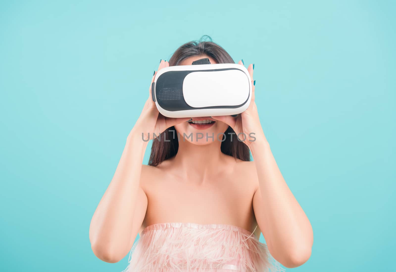 Asian happy portrait beautiful young woman standing smile her using a virtual reality headset, playing on VR glasses device on blue background with copy space for text