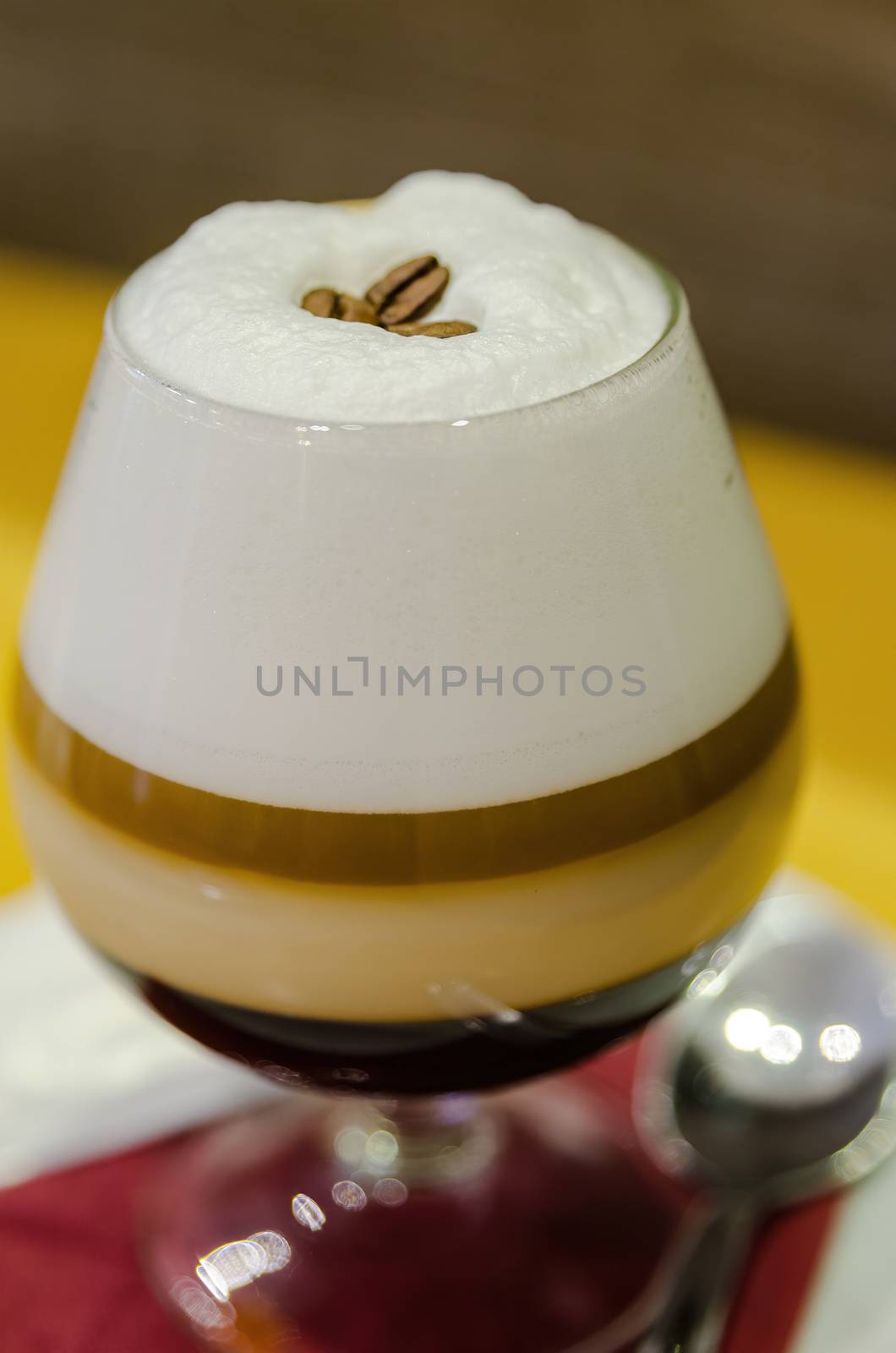 Combination of coffee, cream, milk and whisky in a glass showing the different layers of each ingredient. Decorated with coffee beans, served on a white plate with a coffee spoon