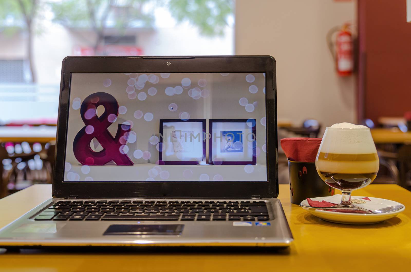 Laptop with wallpaper symbol & and some pictures, on a restaurant table to work while having an Irish coffee