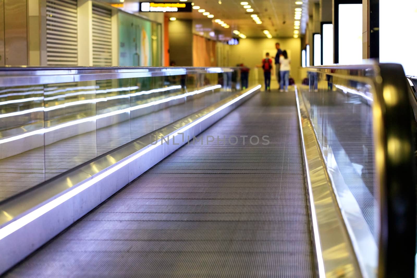 The bright purple transport lane at the airport carries a family of passengers and their luggage blurred along the corridor.